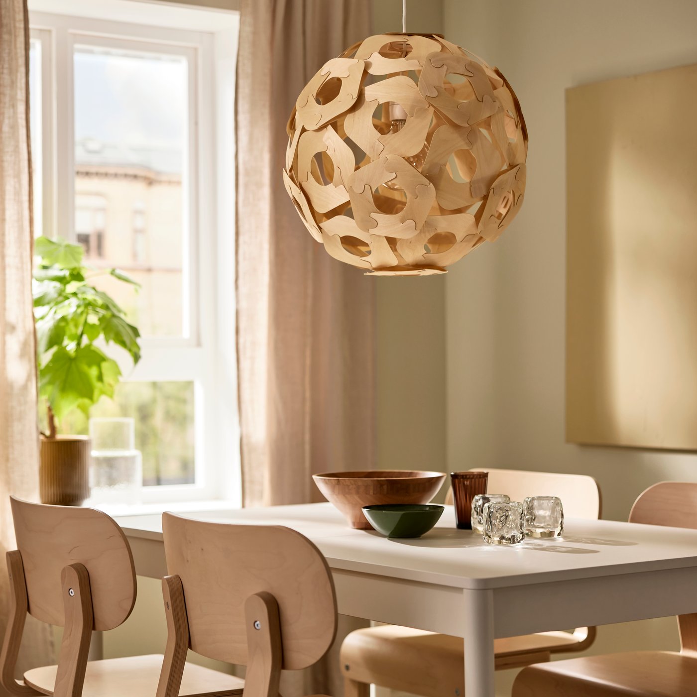 An ÖDLEBLAD pendant lampshade hangs over a dining table and some birch veneer LYCKAN chairs in a dining room.
