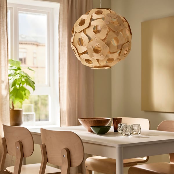An ÖDLEBLAD pendant lampshade hangs over a dining table and some birch veneer LYCKAN chairs in a dining room.