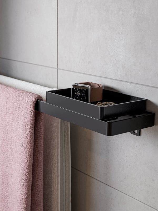 A black towel rail with tray. A white bath towel and a light pink bath towel hang on the rail, and a watch is on the tray.