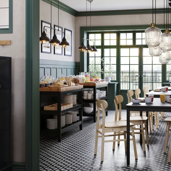 Un bar con pannelli verdi alle pareti e tavoli TOMMARYD, sedie RÖNNINGE in betulla e due isole da cucina VADHOLMA.