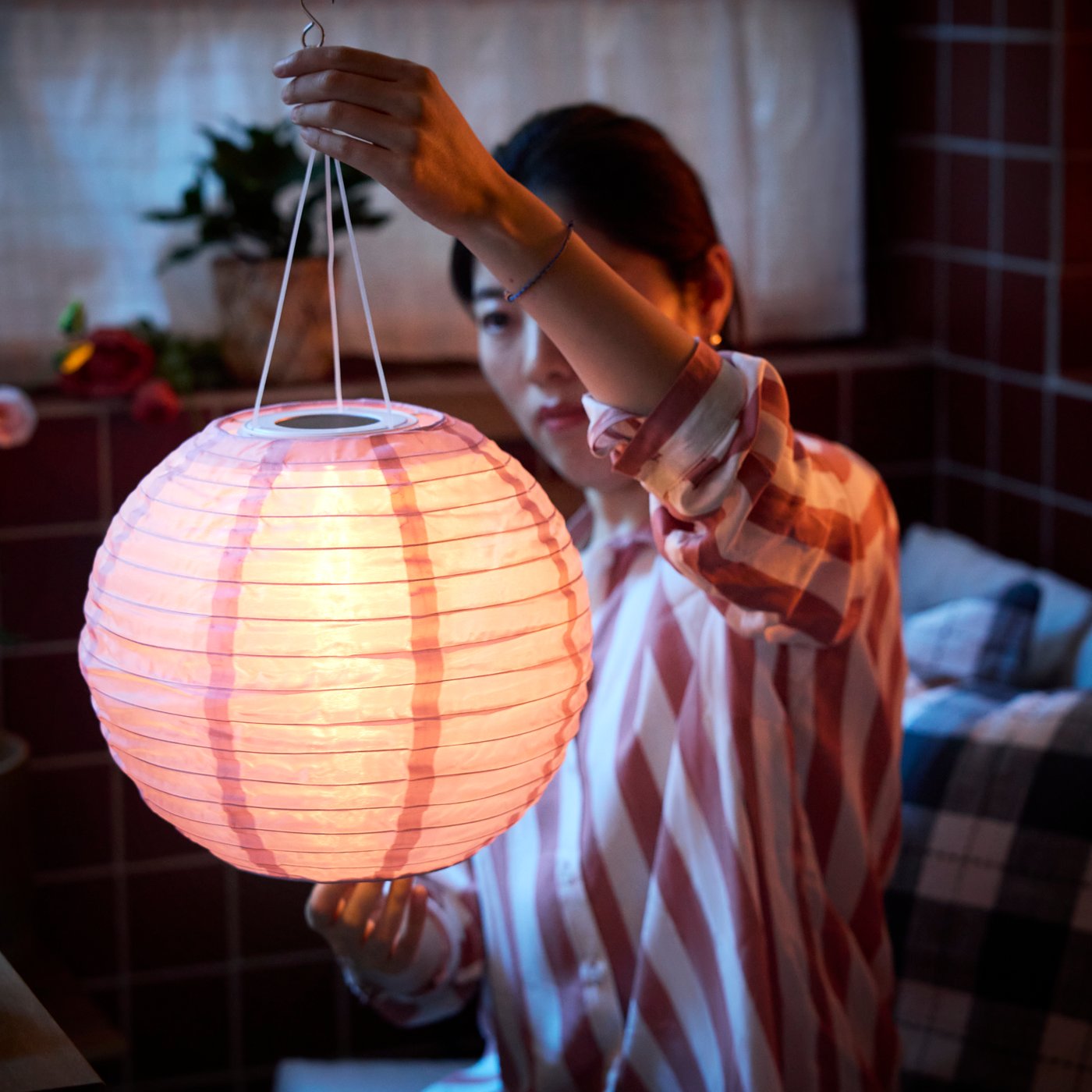 A close-up of a hand holding a pink SOLVINDEN LED solar-powered pendant lamp, featuring a round globe design.