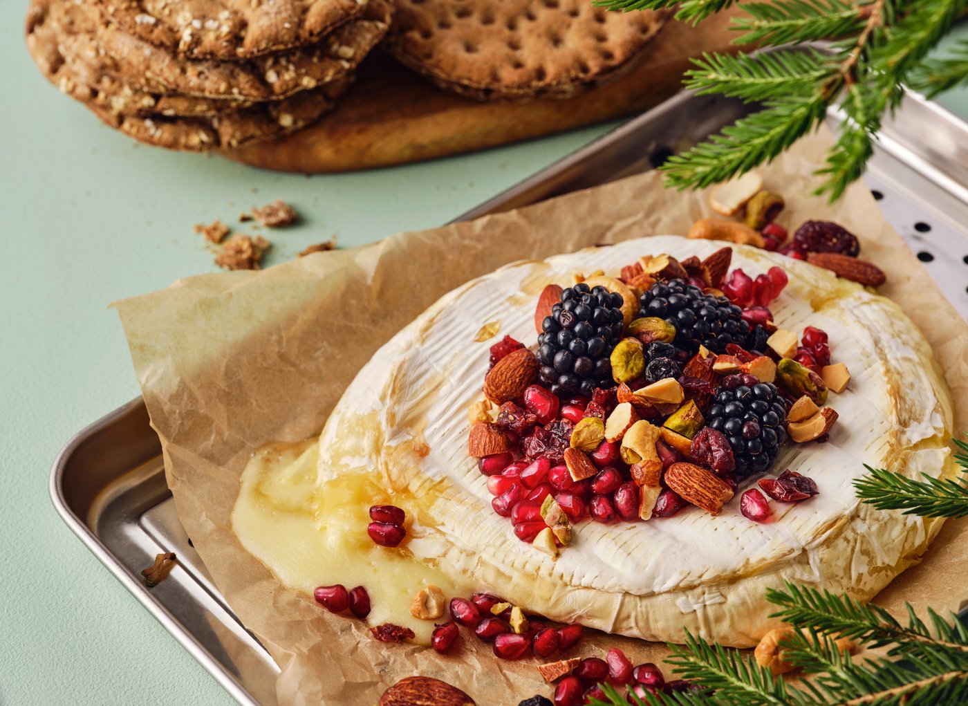 Un brie cuit au four garni de noix, de fruits rouges et de graines de grenade sur une plaque de cuisson.