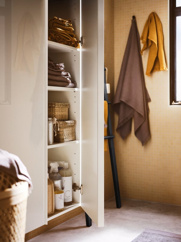 A bathroom with two high-gloss white GODMORGON high cabinets with an open door with towels, boxes and products inside.