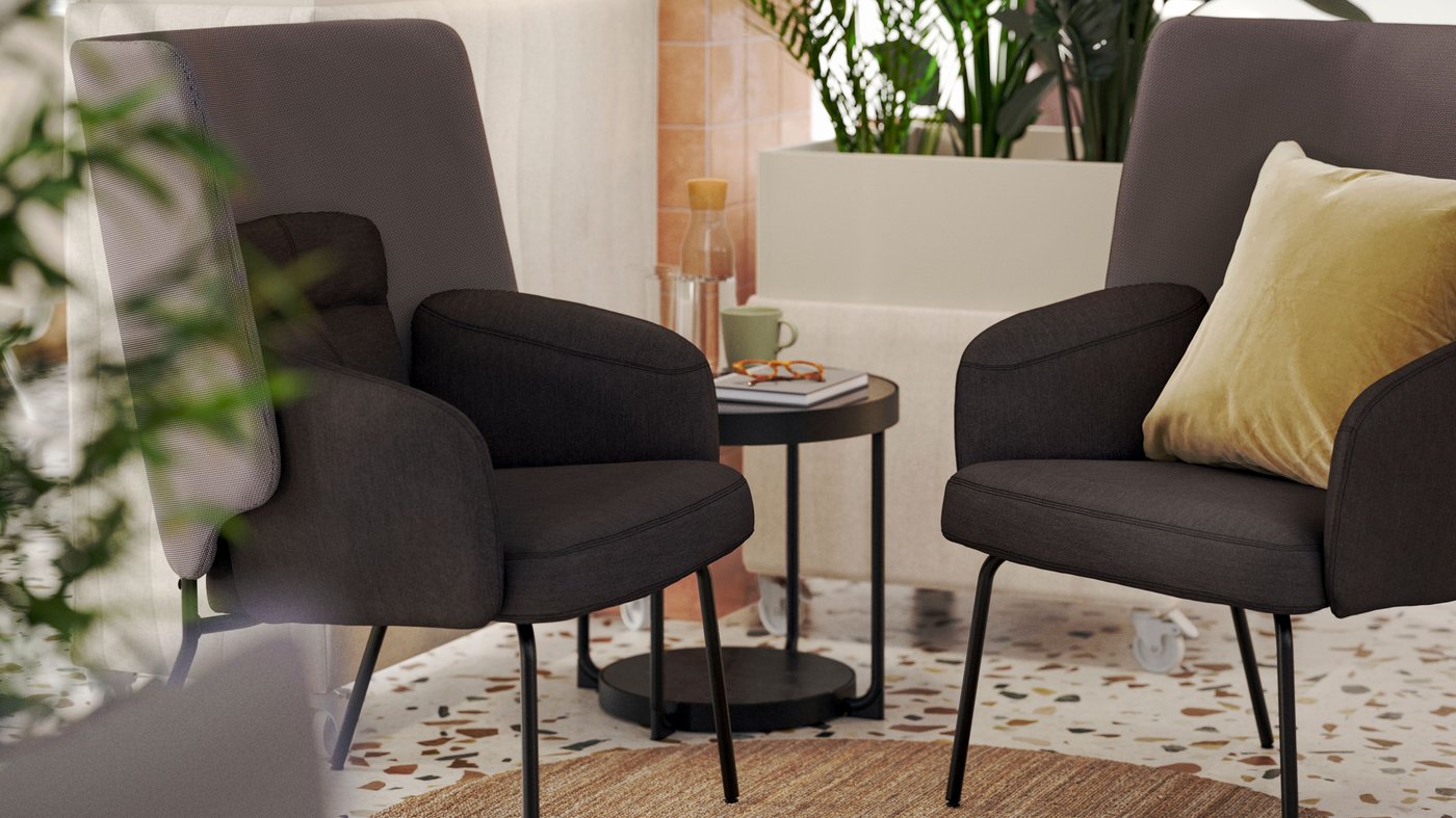 Two modern, dark grey BINGSTA high-back armchairs slightly face each other in a nook-like area within a light-filled lounge.