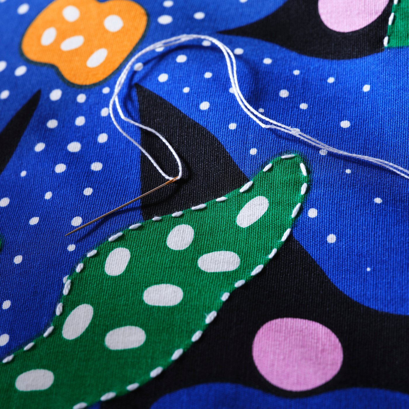 A close-up of the embroidery on the colourful floral pattern of the MÄVINN cushion cover. A needle with thread lies on top.