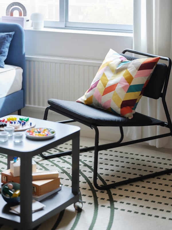A BACKSÄLEN armchair in the corner of a bright living room with a pendant lamp overhead and a coffee table nest beside it.