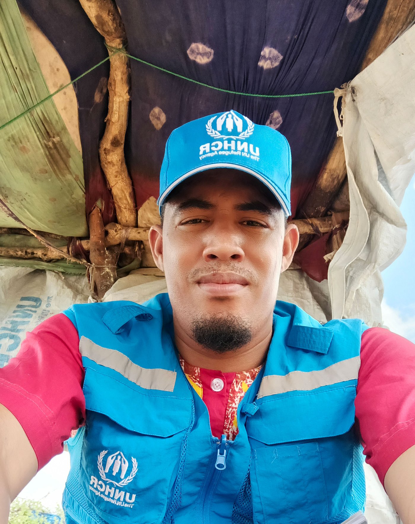 Ilyas steht draussen in einem Unterstand und trägt seine blaue UNHCR-Arbeitsuniform.