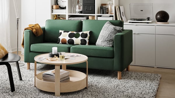 Cozy living room corner featuring a green two-seater sofa, playful cushions, a light wooden coffee table, and a modern shelf with a turntable.