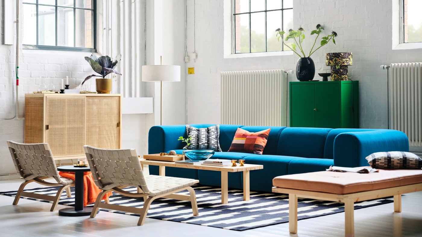A living room with a dark turquoise STOCKHOLM 2025 4-seat sofa, easy chairs, and a floor lamp arranged around a coffee table.