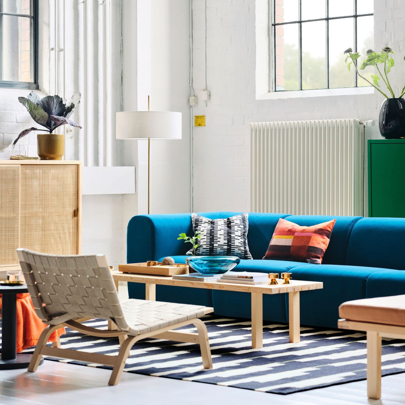 Es ist ein Wohnzimmer mit einem STOCKHOLM 2025 4er-Sofa in Dunkeltürkis, Sesseln und einer Standleuchte zu sehen, die alle um einen Couchtisch angeordnet sind.