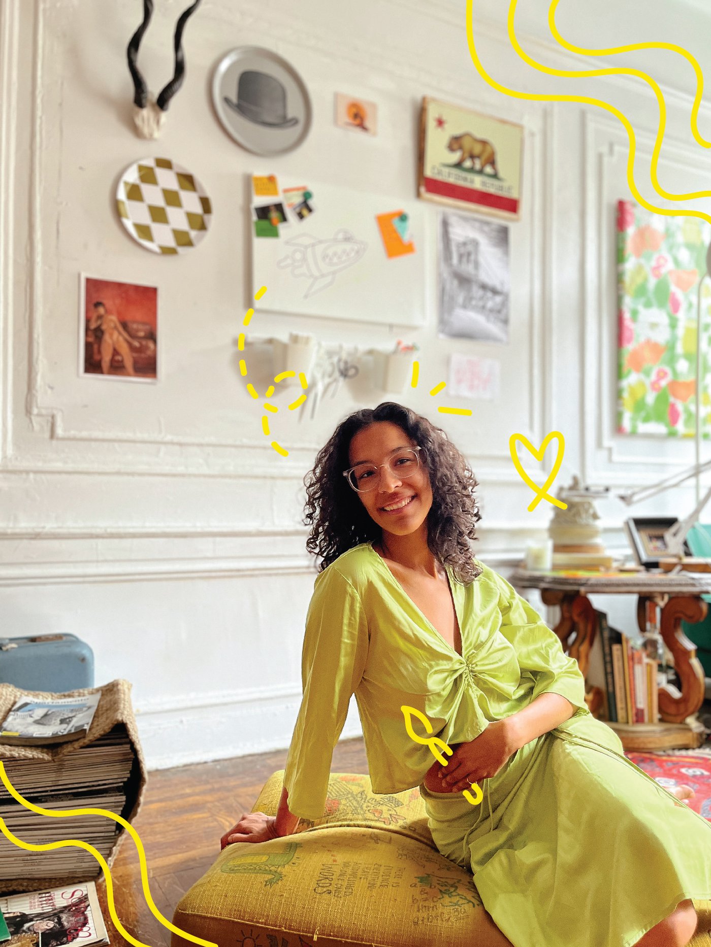 A woman in a green dress sitting on a floor cushion, with drawing and painting equipment pictured behind her.