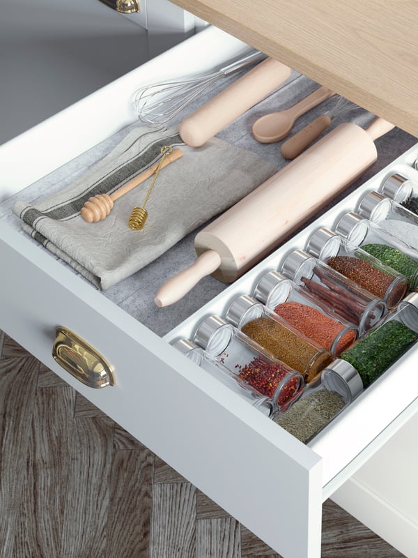 An opened KNOXHULT drawer with ÖRTFYLLD spice jars filled with colourful spices, honey drips and baking accessories.