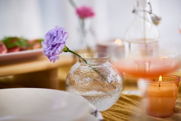 In a small, bulbous vase stands a single purple carnation at an angle.