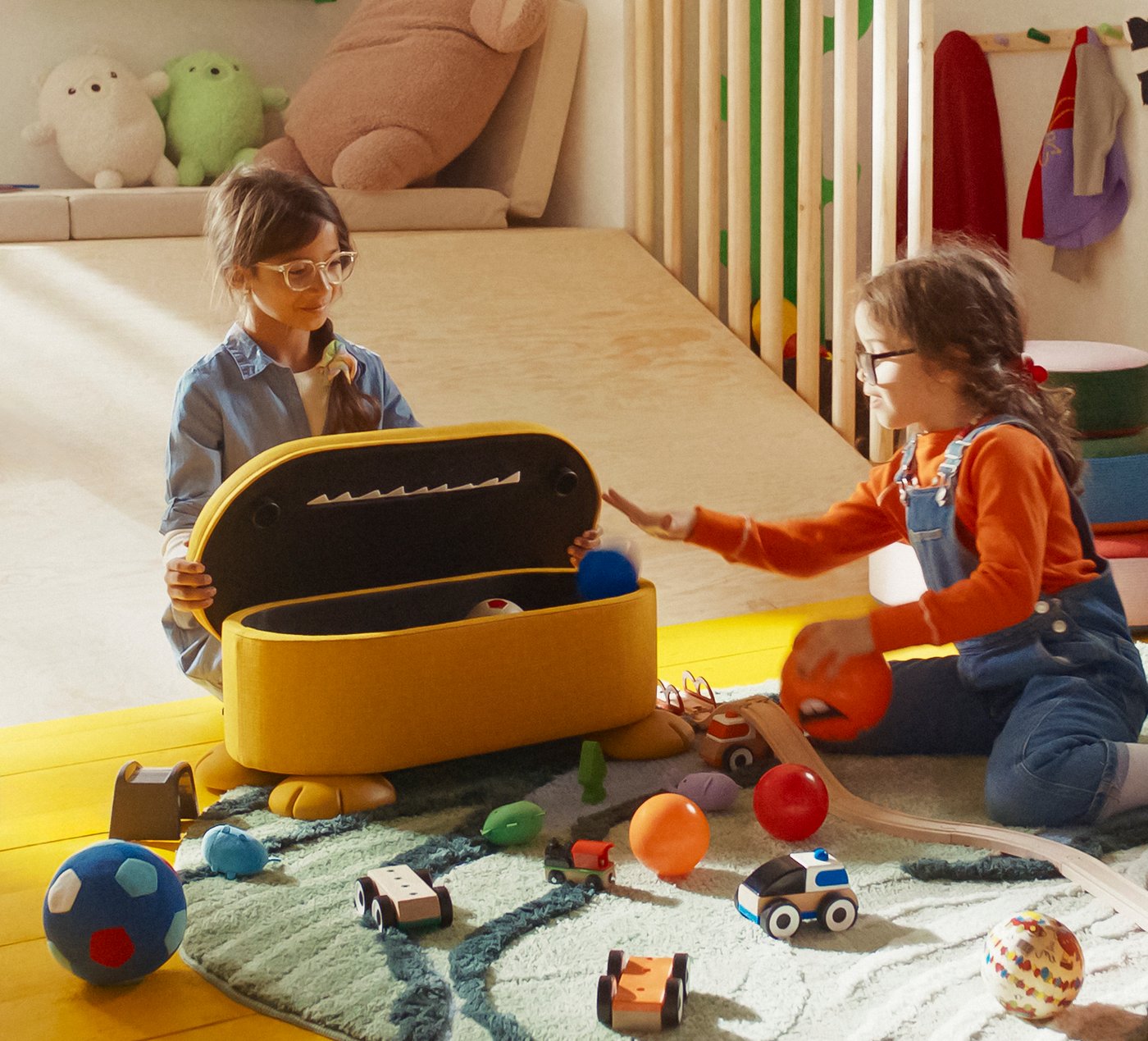 Ein gelber GREJSIMOJS-Sitzhocker mit Stauraum im Kinderzimmer, mit dem 2 Mädchen spielen.