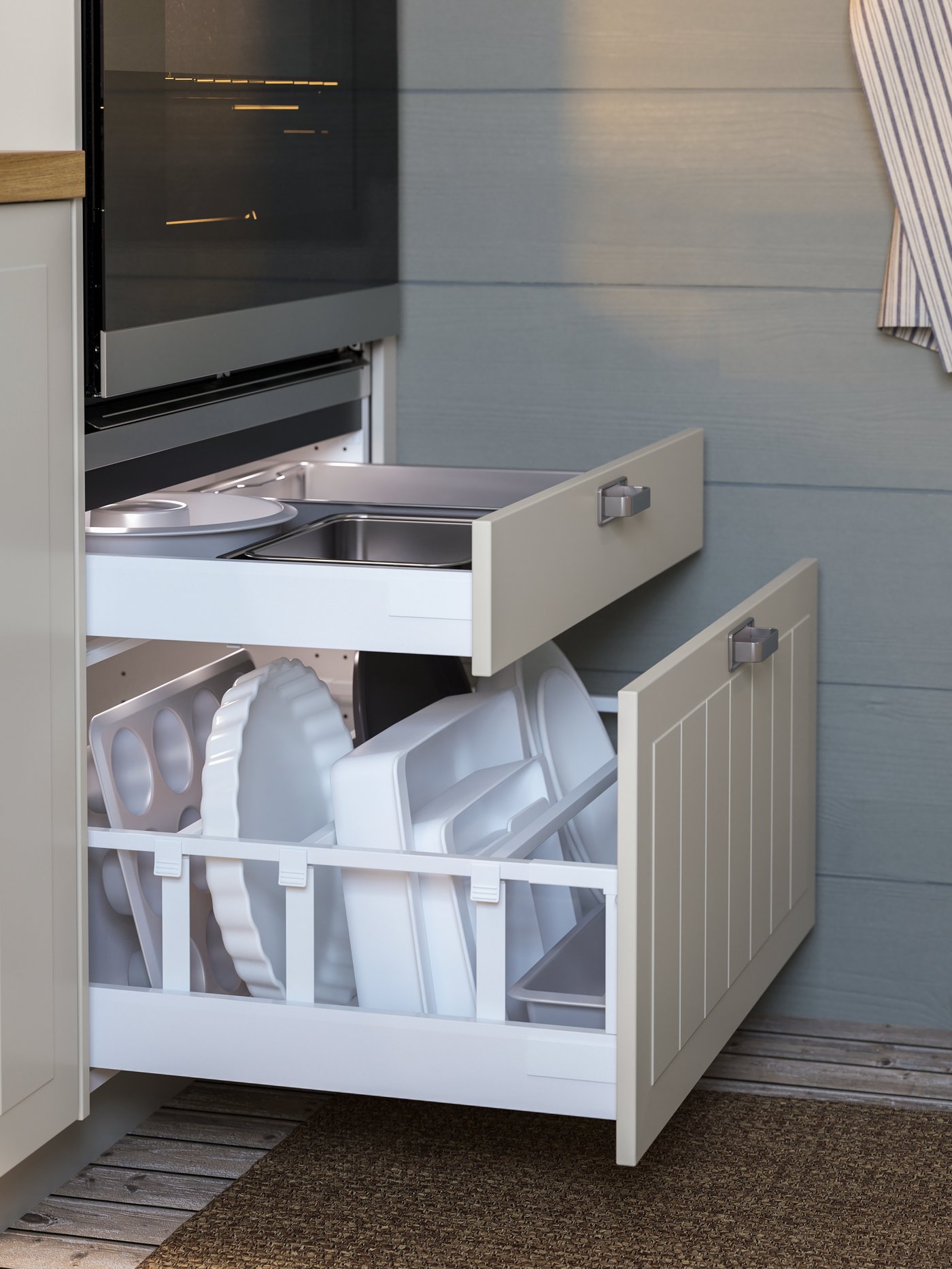 Two open beige drawers below the oven with baking trays, white form moulds and drawer dividers.