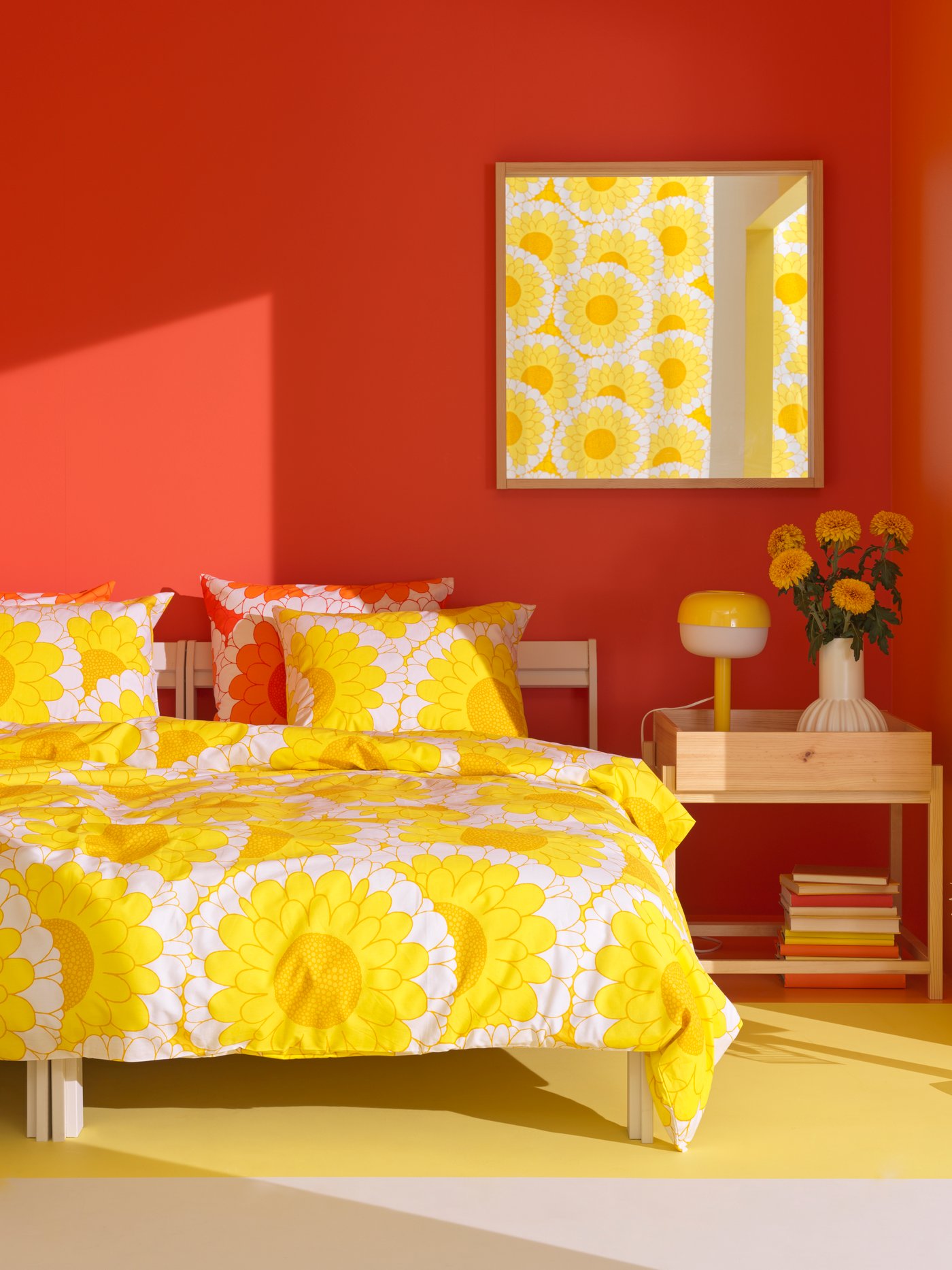 Bilik tidur berwarna jingga-merah dengan lantai berwarna kuning mempunyai katil dengan linen katil KRANSMALVA bercorak bunga matahari yang besar berwarna kuning terang.