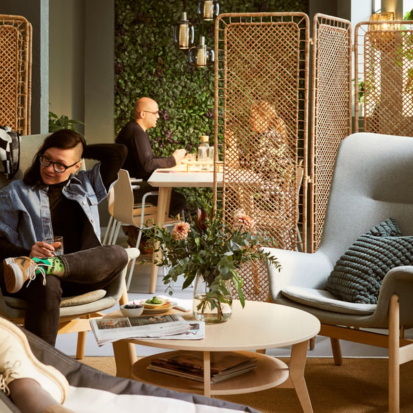 A spacious room with light-green VEDBO armchairs around a JAKOBSFORS coffee table. Artificial plants cover the far wall.