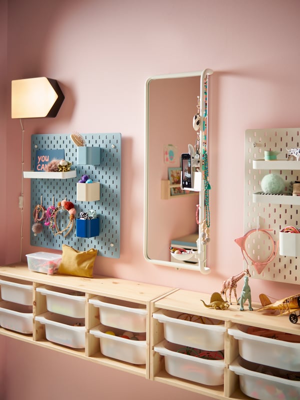 Part of a children’s room showing a tall mirror and pegboards on the wall and below plenty of easy-access pull-out storage.
