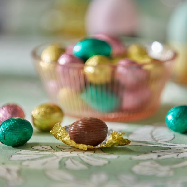 Bol rose avec des œufs en chocolat au lait posé sur une nappe verte à motifs fleuris.