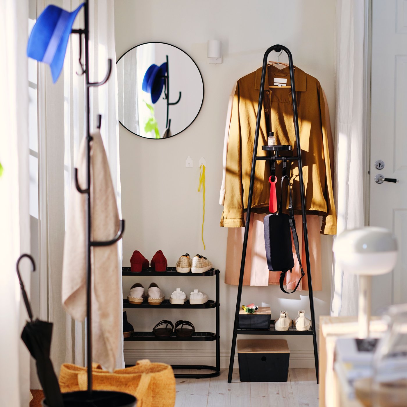 A black ÄLGANÄS shoe rack holding several pairs of shoes with a mirror above it, by an ÄLGANÄS coat rack with shoe storage.