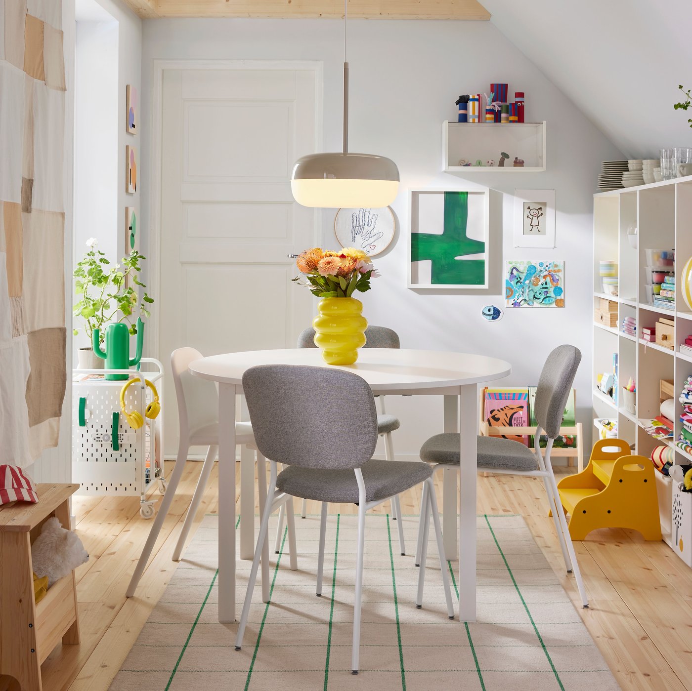 A bright dining area with a round table surrounded by four VIHALS chairs in white beige-grey, illuminated by a pendant light.