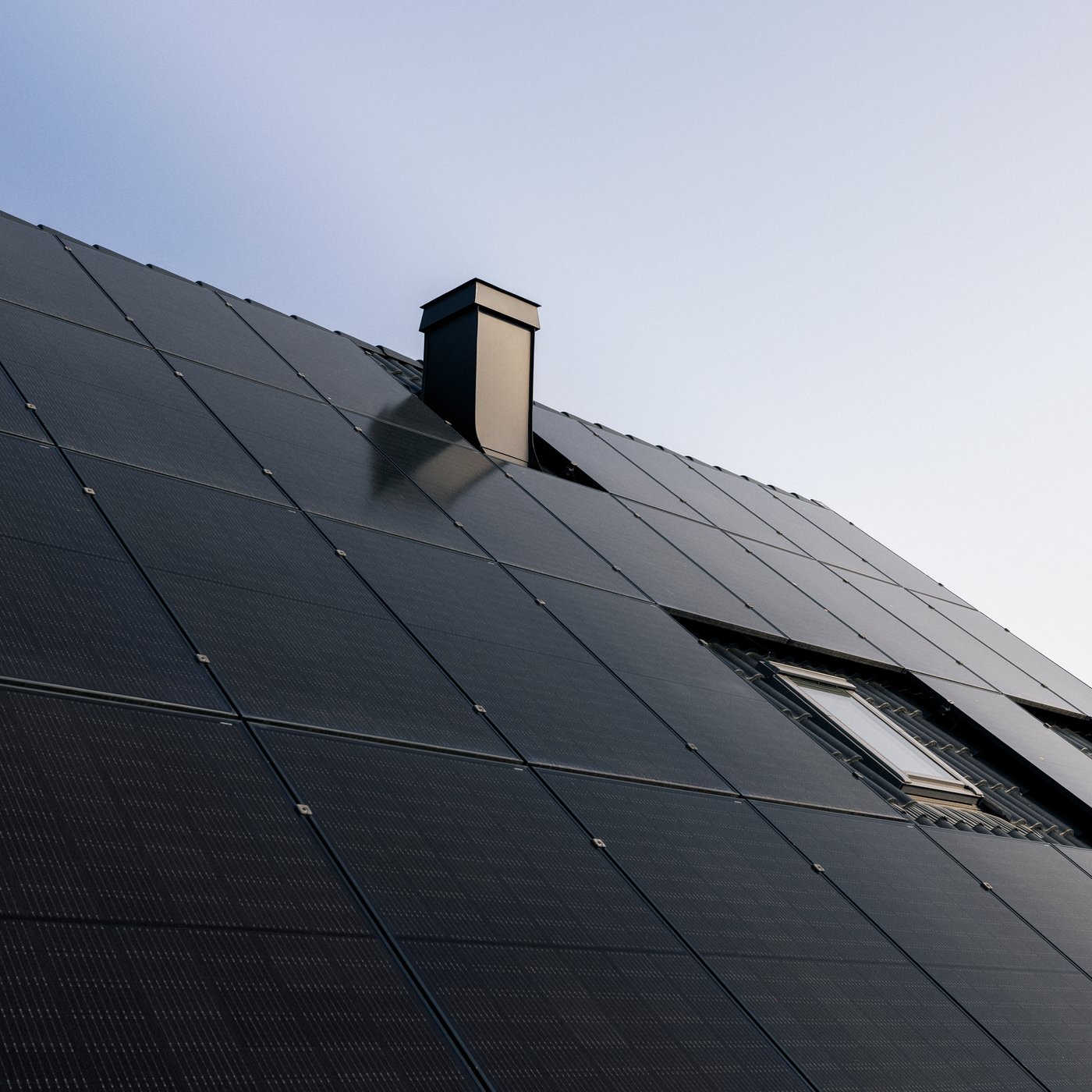 Krov prekriven elegantnim crnim solarnim panelima s dimnjakom i prozorom pod vedrim nebom.