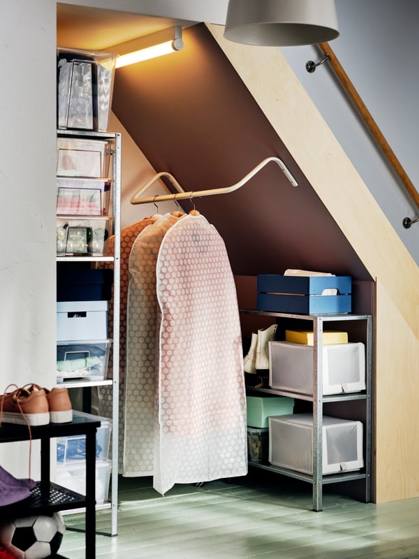 A storage space under the stairs with a MULIG clothes rack holding garment bags filled with clothing.