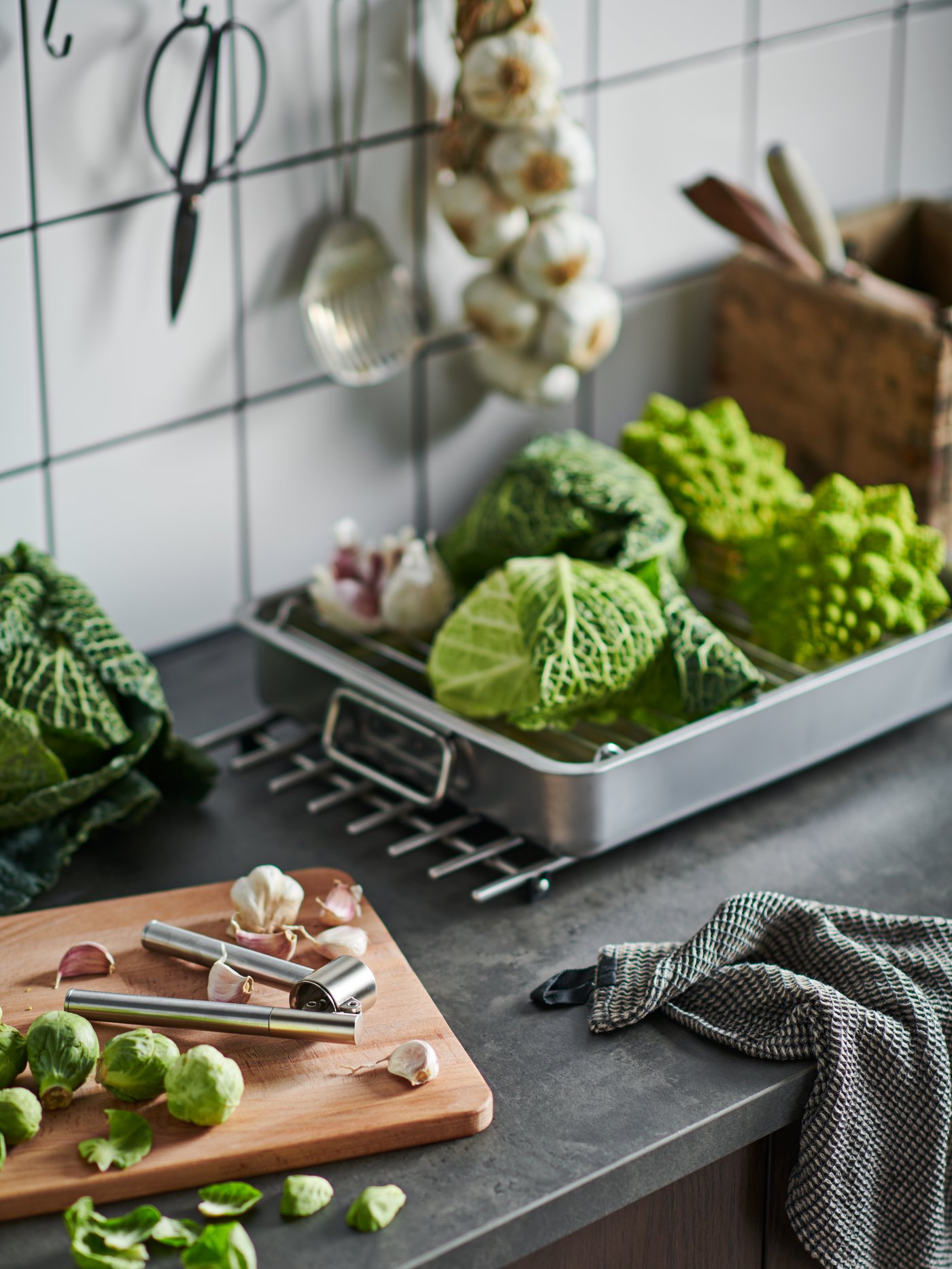 Various IKEA KONCIS cooking tools in stainless steel hung on a red tilled wall.