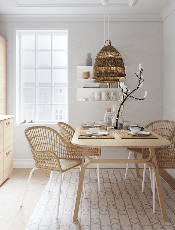 Ein Esszimmer im nordischen Stil mit dezenten Farben, viel natürlichen Materialien und blondem Holz. Zum skandinavischen Esstisch gesellen sich geflochtene Rattansessel.