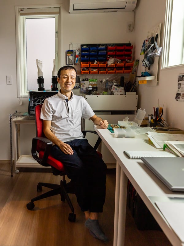 A smiling man sits in an office sopacem surrounded by neatly organised things on the wall.
