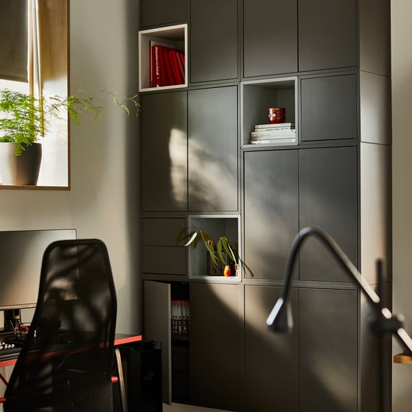 A room with one wall covered with dark-grey EKET cabinets with doors on a wall. Nearby is a gaming desk and gaming chair.
