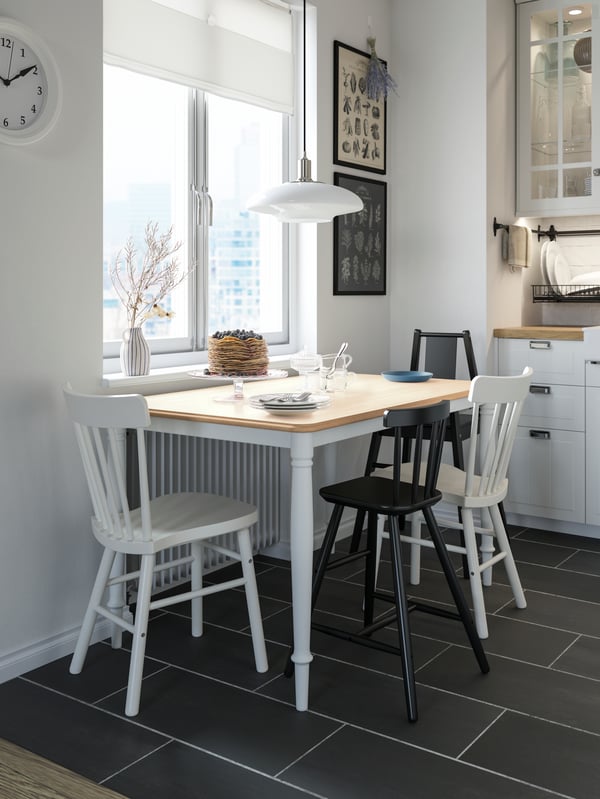 A blueberry pancake cake on a dining table by a window, four chairs, a pendant lamp, tableware and cutlery.