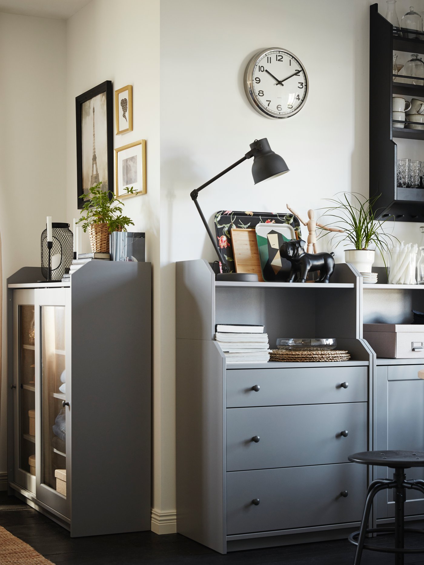 A grey HAUGA cabinet with 2 doors sits around the corner from a grey HAUGA chest of 3 drawers with shelf.