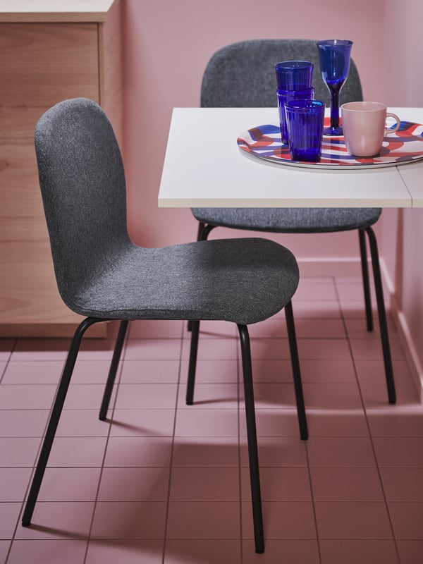 Two chairs formed by black SEFAST underframes and medium-grey KARLPETTER seat shells by a small table in a pink-tiled room.