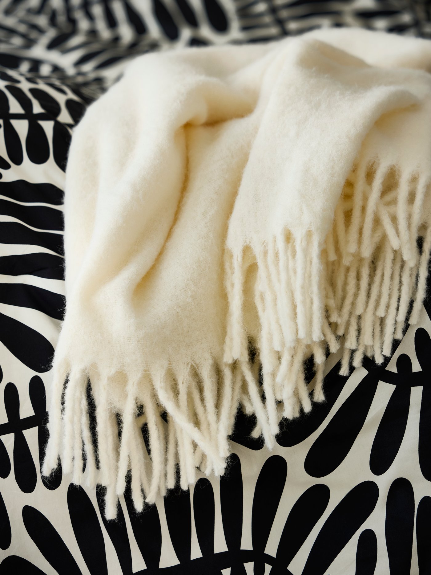 Close-up of off-white KLIPPOXEL throw on top of black and white MAJSMOTT comforter.