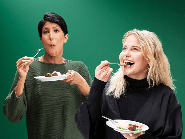 Zwei Personen halten Teller mit einem Gericht und essen gemeinsam vor grünem Hintergrund.