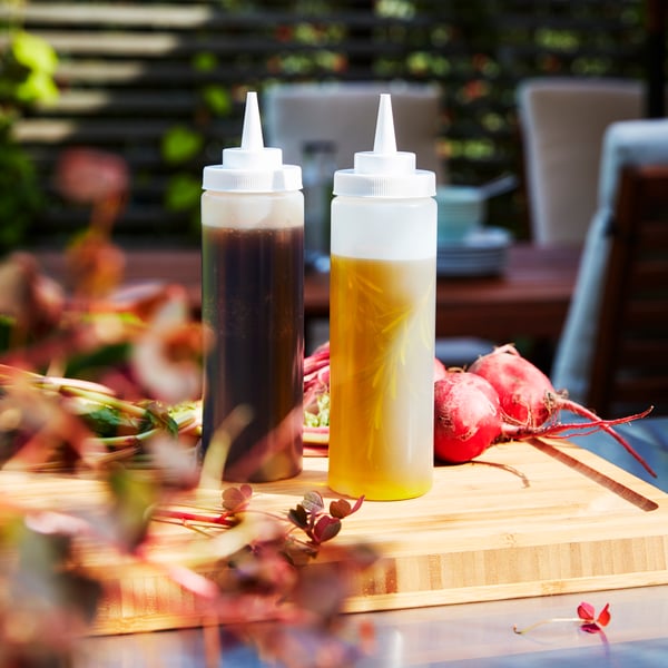 Two GRILLTIDER squeeze bottles in transparent plastic holding condiments on a wooden chopping board with items of food.