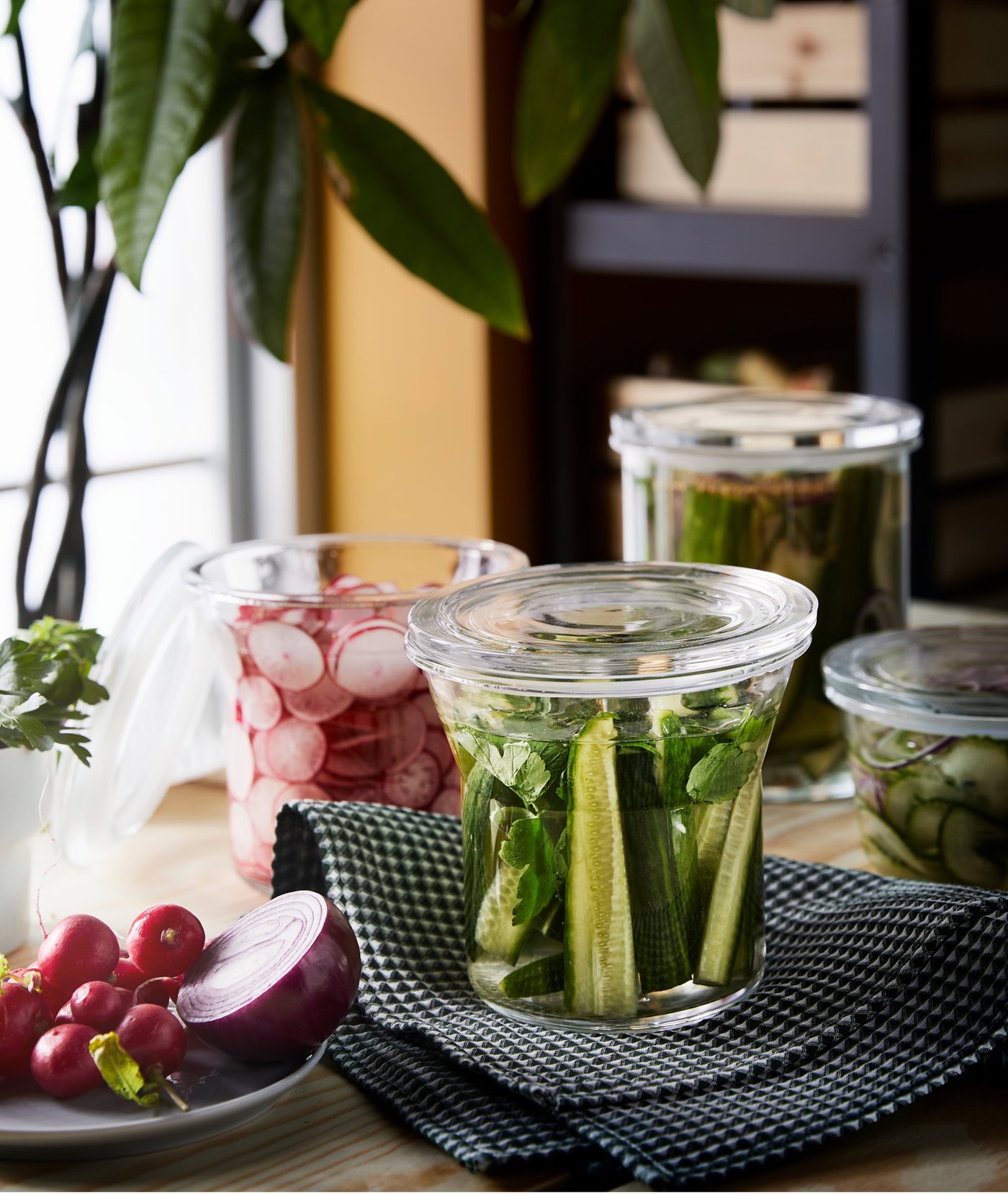 Several glass jars sitting on a table filled with various vegetables and a plate with more vegetables beside them.