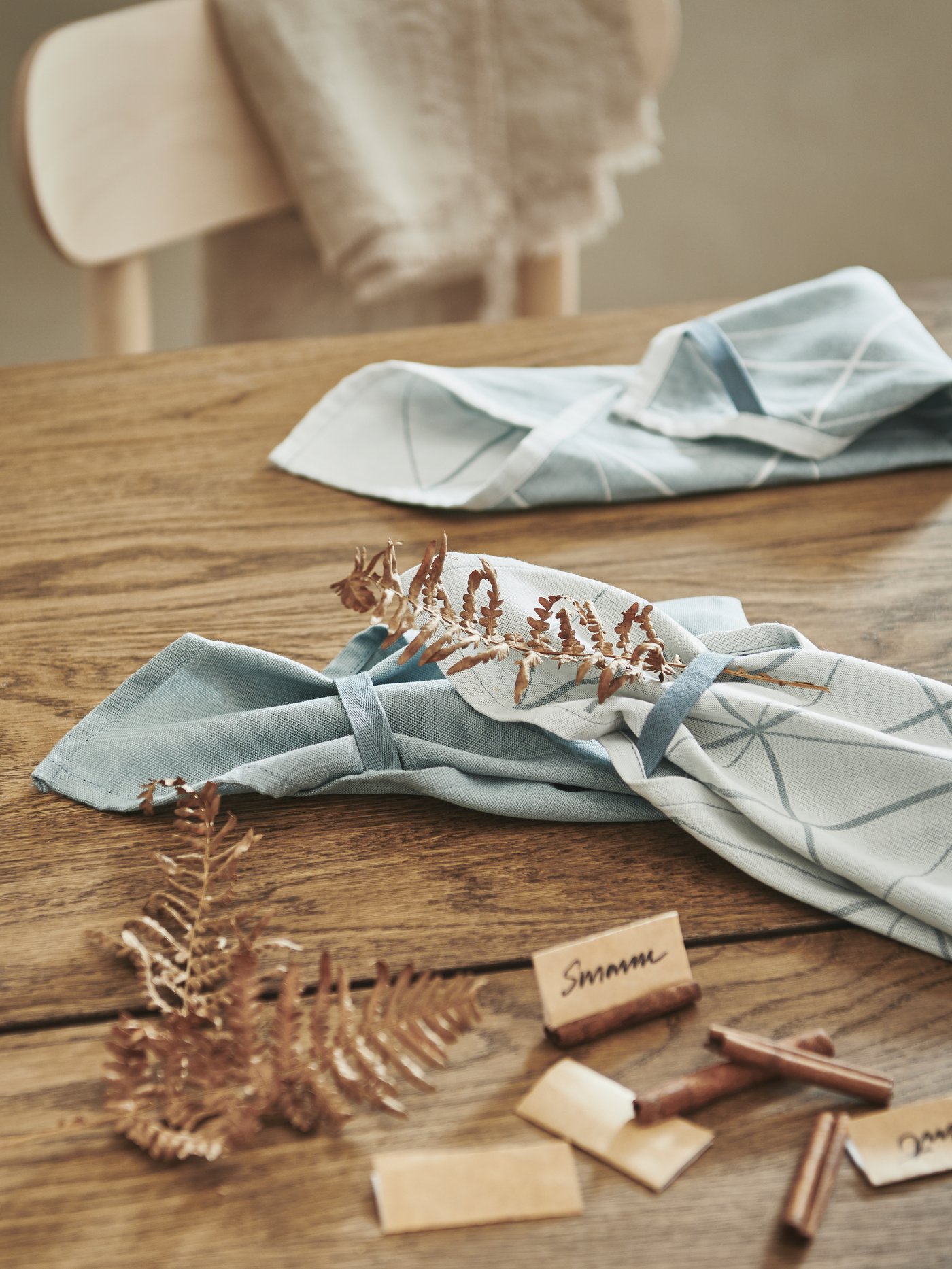 A wooden tabletop being prepped for a party, with decorations, handwritten name signs and folded, blue SANDVIVA tea towels.