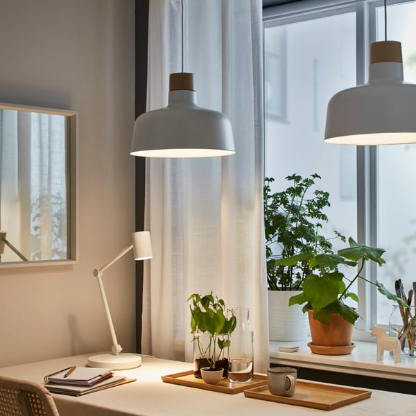 Two BUNKEFLO pendant lamps above a MELLTORP dining table with a NYMANE Table lamp and other accessories including a tray with plants, some plant pots and a VOXLOV dining chair at the table. 