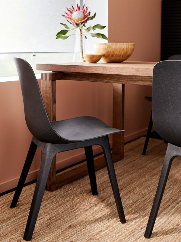 A dining room with chairs in anthracite, a jute rug and a stained oak veneer table holding bowls in bamboo and a vase.