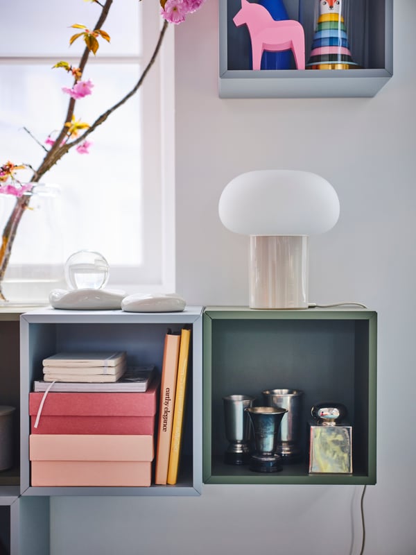 One green and one light blue EKET cube cabinet hanging on a wall with a DEJSA lamp placed on top of them.