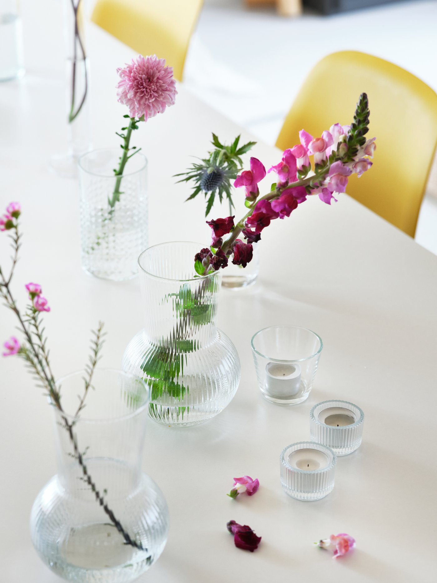 På et bord står der forskellige vaser med blomster i og sterinlys i glasstager.
