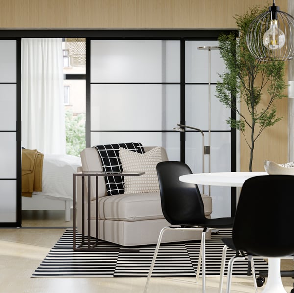 Im offenen Wohnbereich einer minimalistisch eingerichteten Wohnung sind ein Esstisch, Stühle und Sessel vor SKYTTA Schiebetüren zu sehen.