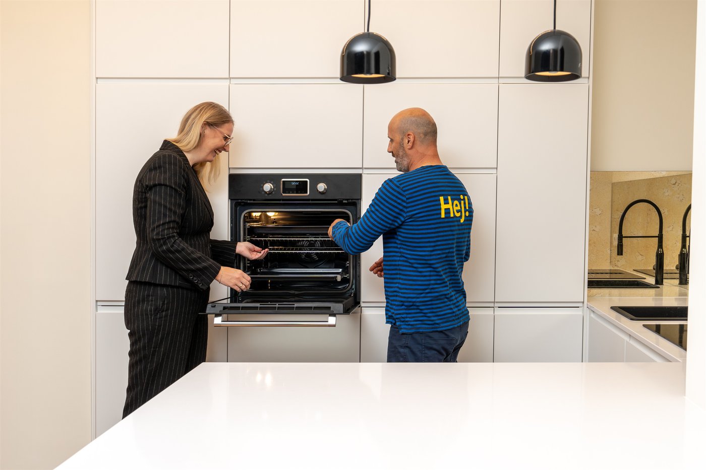 Man sieht eine Frau und einen IKEA Mitarbeiter wie sie den Backofen in einer weißen IKEA Küche öffnen und miteinander sprechen.