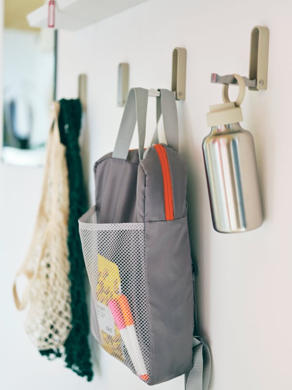 Wall section with three KLYKET hooks, two of which hold clothes and accessories, the third is in its folded-up position.