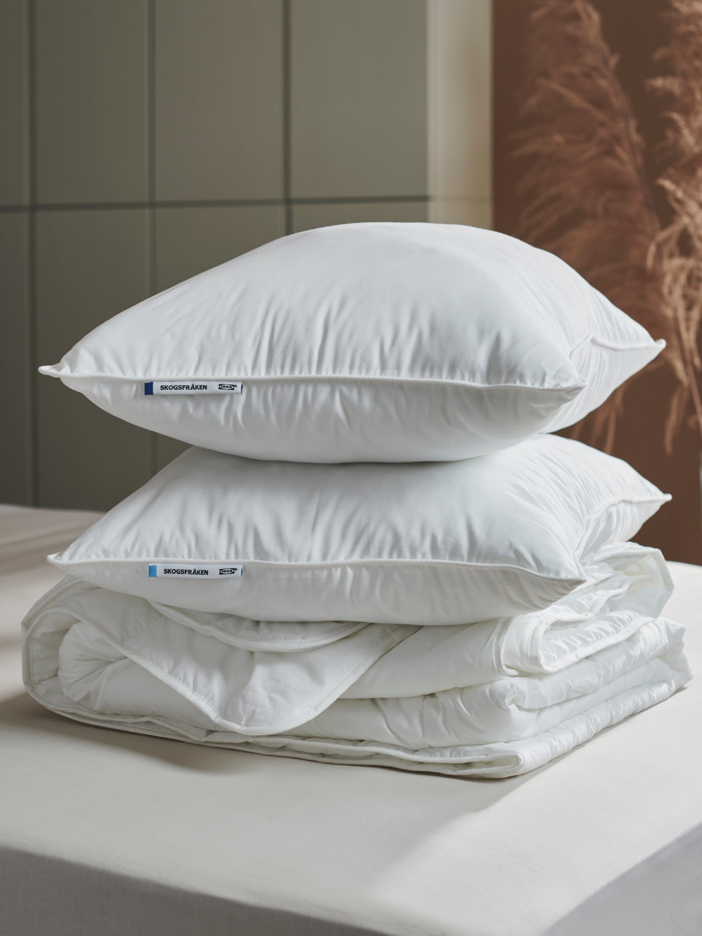 Two different SKOGSFRÄKEN pillows are piled on top of each other on top of a folded STJÄRNBRÄCKA duvet on a bed.
