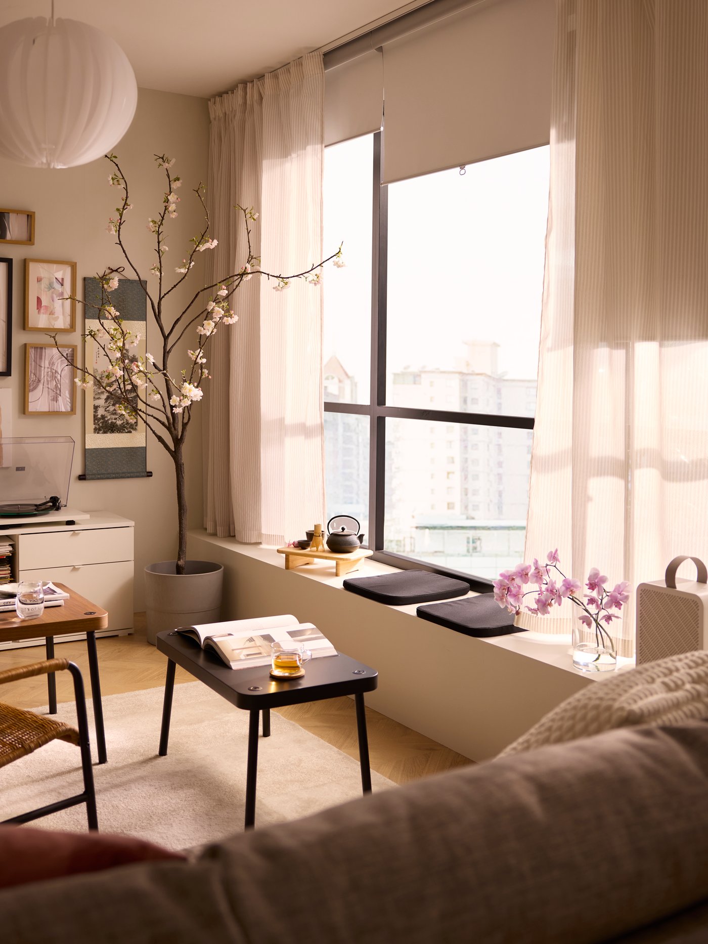 A large sunlit window with TRETUR block-out roller blinds and BYMOTT curtains. Next to it are SONHULT nesting tables.