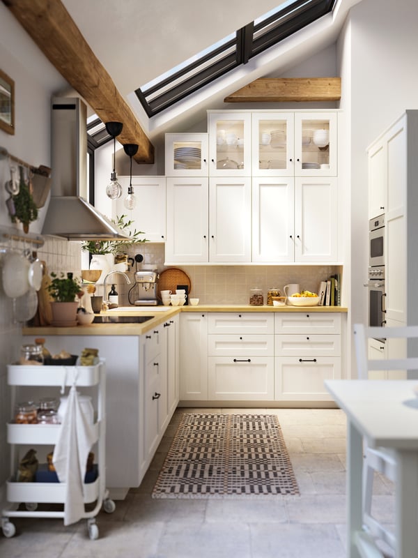 A kitchen with ENKÖPING white wood-effect kitchen fronts, a MATMÄSSIG induction hob and a wall-mounted extractor hood.