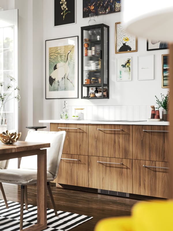 A kitchen with TISTORP fronts with a brown walnut effect and a MOSSJÖN wall cabinet with shelves and glass door.